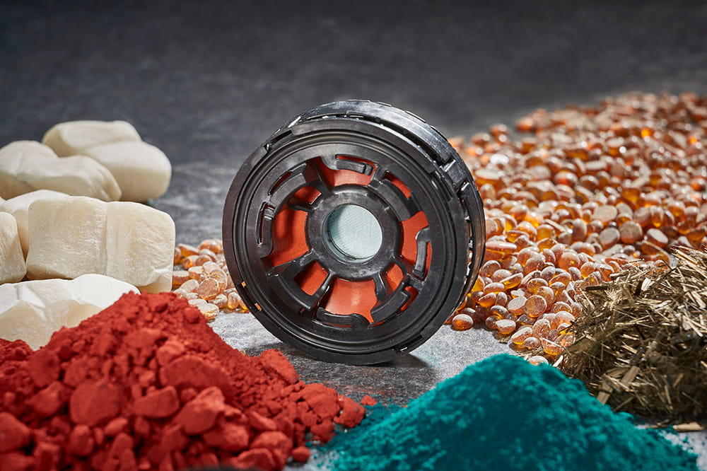 Black circular part surrounded by piles of colored powders and raw materials.